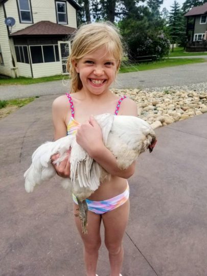 Young girl in swimsuit proudly holding a white chicken