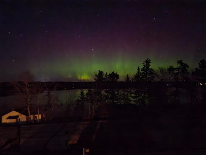 Vibrant aurora borealis over trees and small building at night