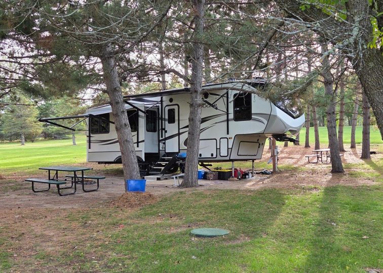 Fifth-wheel RV parked at shaded campsite among pine trees